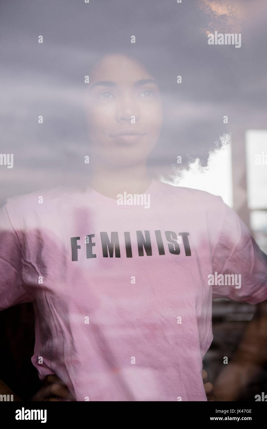 African American donna femminista che indossa la t-shirt dietro la finestra Foto Stock