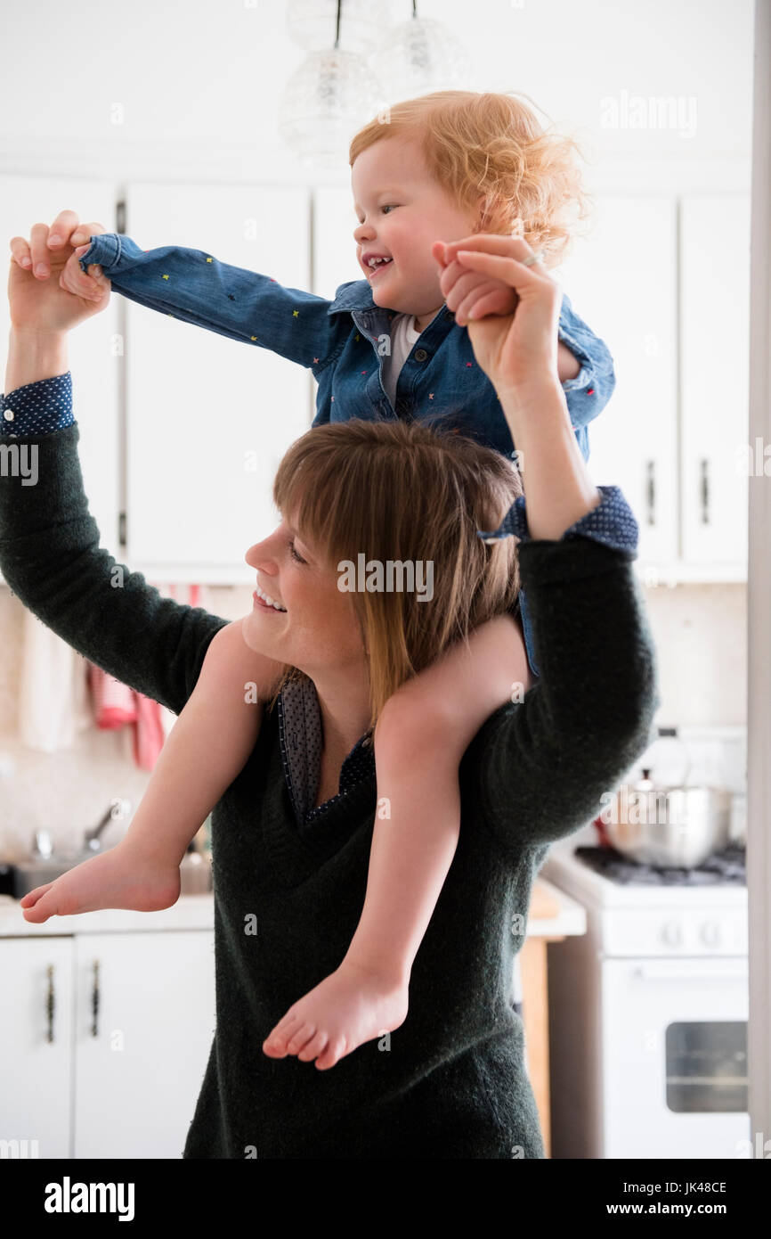 Madre caucasica portando figlia sulle spalle in cucina Foto Stock
