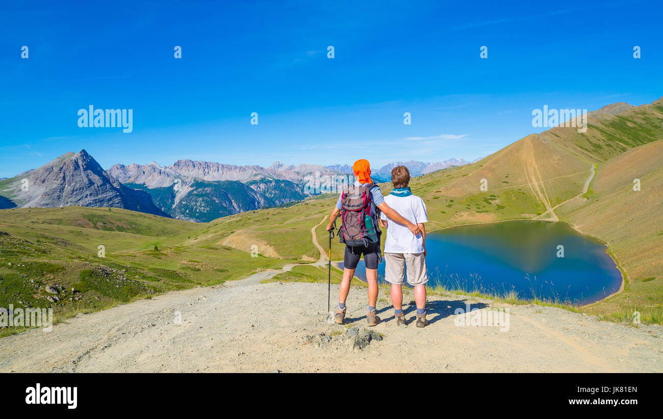 Paio di escursionista sulla cima della montagna guardando il lago blu e picchi di montagna. Avventure estive sulle Alpi. Ampio angolo di visione da sopra. Foto Stock