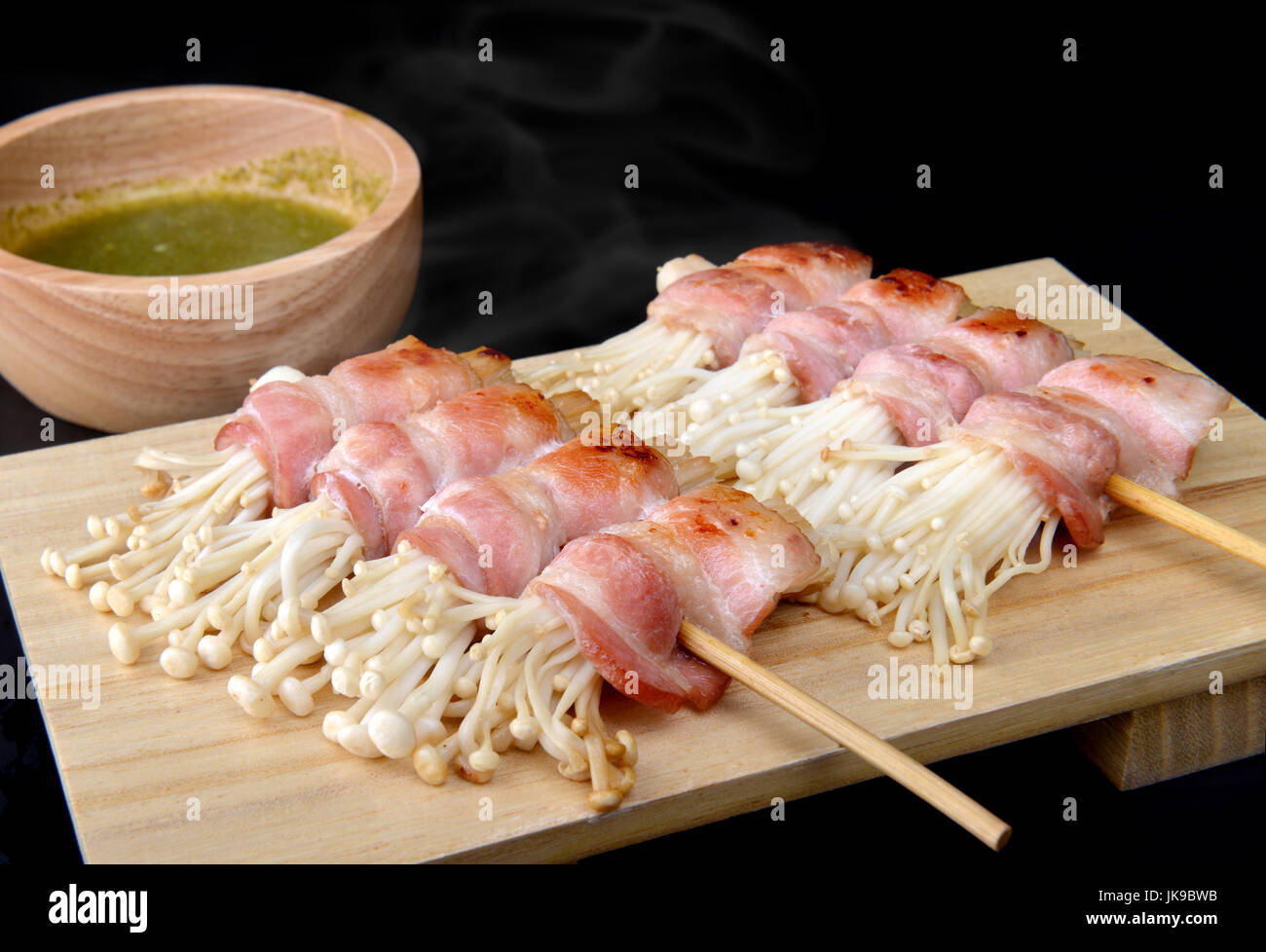 Rotolo di pancetta con funghi enoki alla griglia con sale e la salsa in stile Giapponese impostato sul piatto di legno. Foto Stock