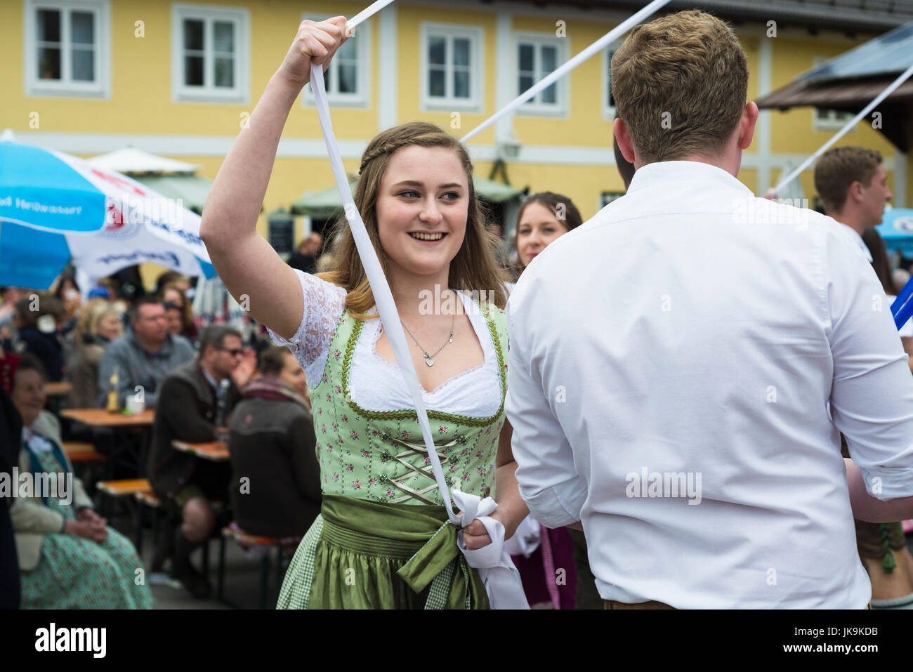 Giovane donna nel tradizionale dirndl e partner maschile nastri di tenuta durante l'esecuzione tradizionale danza folk Bandltanz intorno al maypole Foto Stock