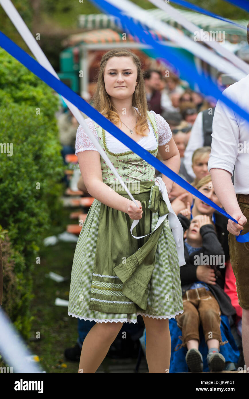 Giovane donna bavarese nel tradizionale dirndl holding nastro bianco mentre si eseguono tradizionale danza folk Bandltanz intorno al maypole Foto Stock