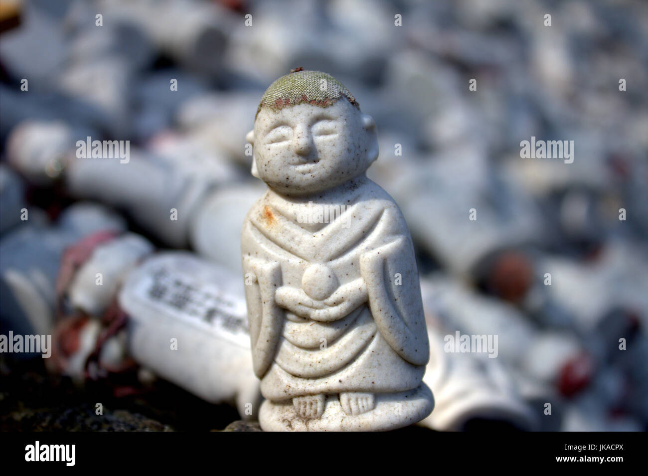 Una piccola statua buddista si siede di fronte a un grande mucchio di statue simili. Foto Stock