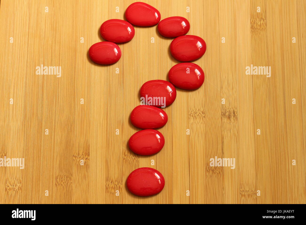 Un punto interrogativo realizzata con ciottoli di rosso in stile Zen su un marrone pavimenti in bambù Foto Stock