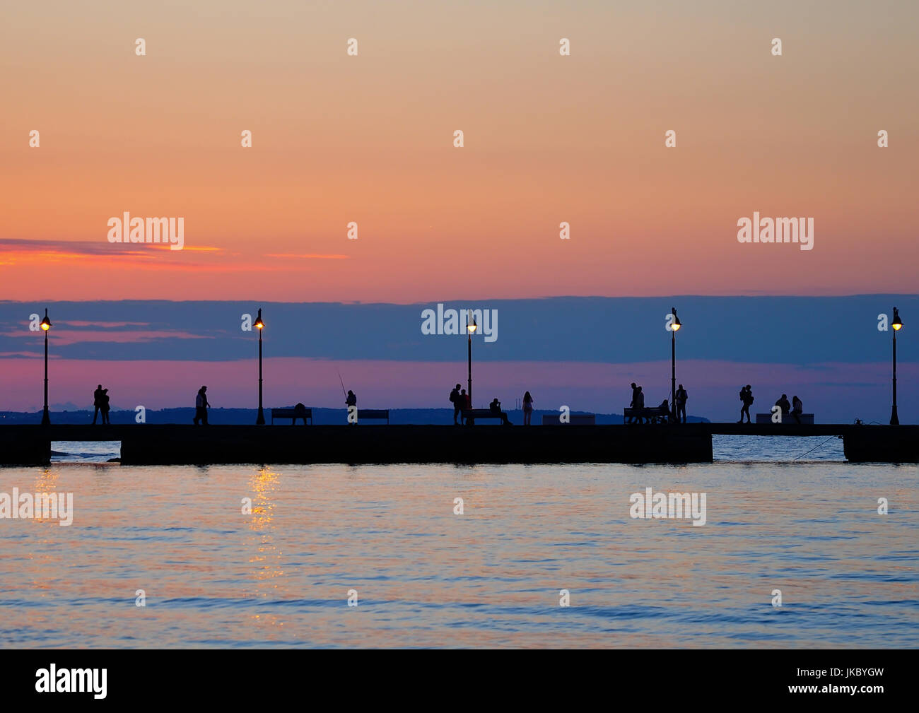 Sagome umane camminando sul dock al tramonto Foto Stock