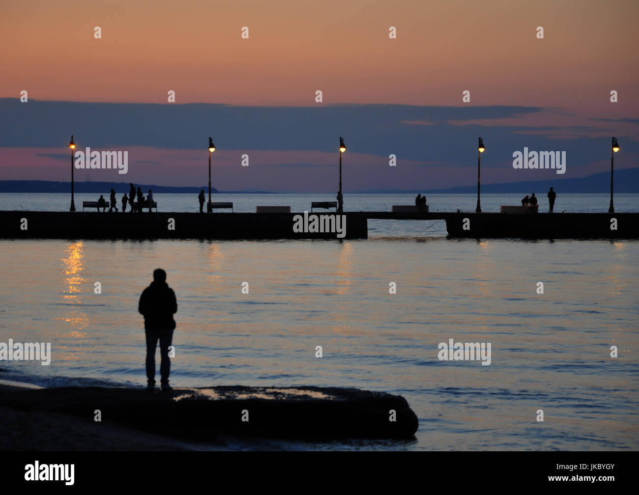 Sagome umane camminando sul dock al tramonto Foto Stock