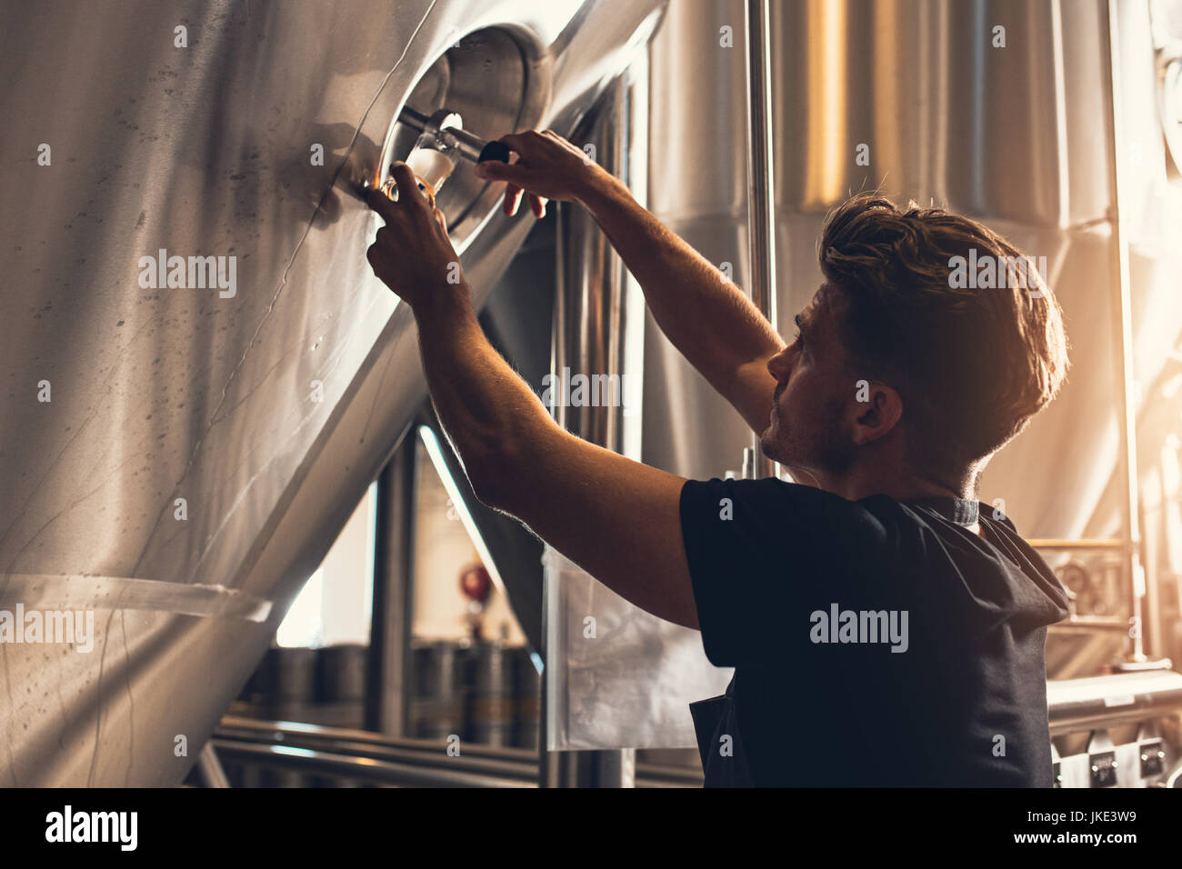 Il birraio e la chiusura del portello della birreria serbatoio. Giovane maschio dipendente che lavora in beer manufacturing factory. Foto Stock