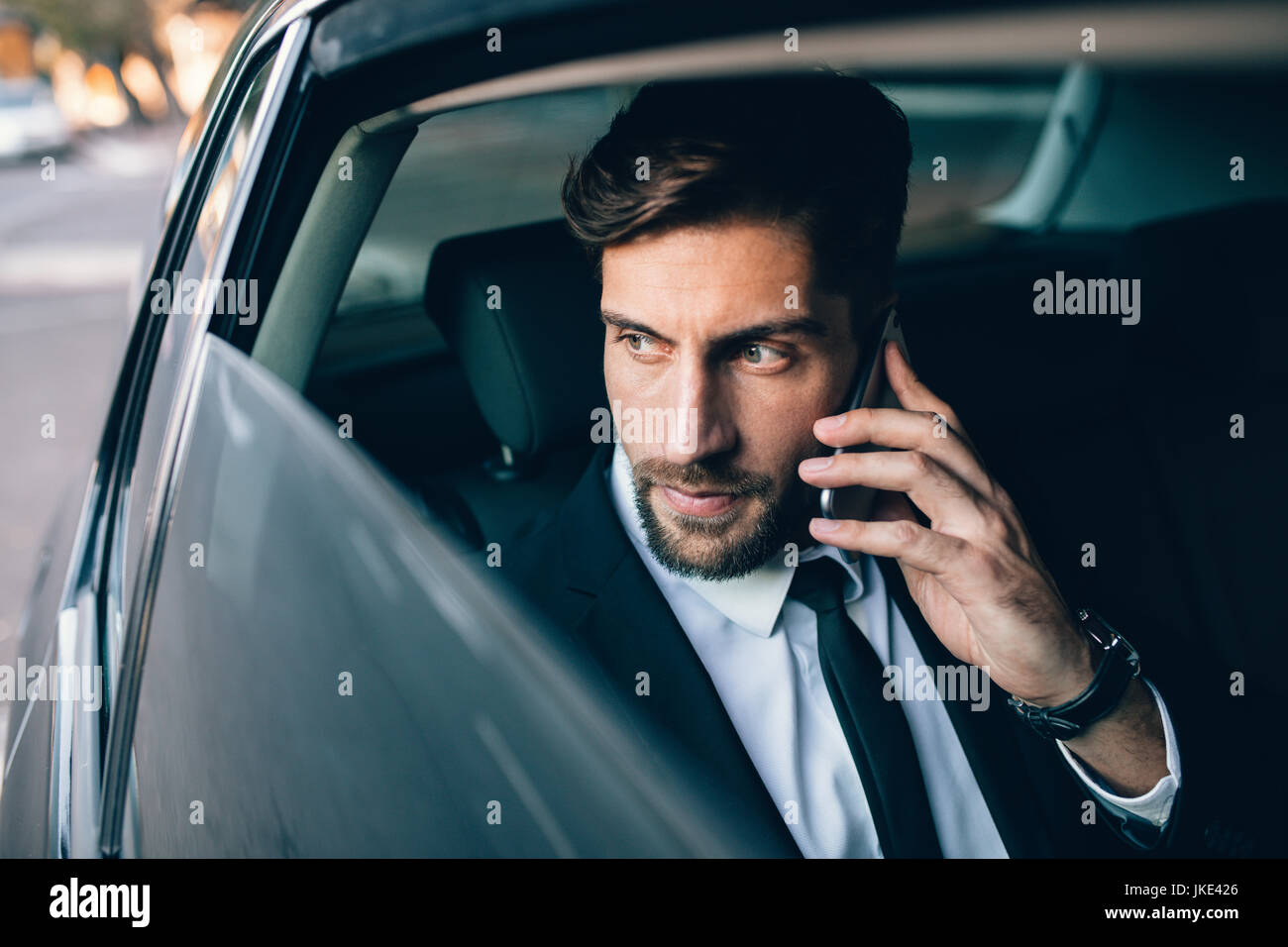 Imprenditore parlando al telefono cellulare e guardando fuori dalla finestra mentre è seduto sul sedile posteriore di un taxi. Maschio di business executive che viaggiano da un c Foto Stock