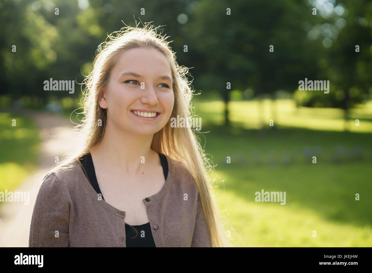 Teen ragazza sorridente nel parco verde nella soleggiata sera d'estate Foto Stock