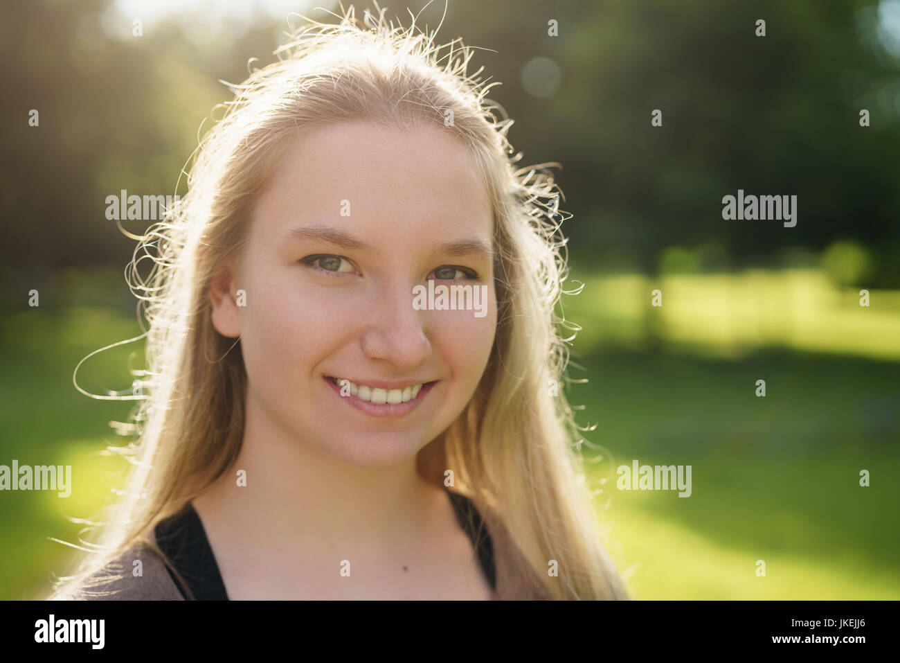 Teen ragazza sorridente nel parco verde nella soleggiata sera d'estate Foto Stock