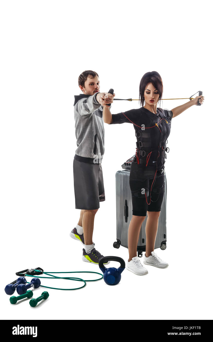 Elettrici di stimolazione muscolare donna fitness in pieno ems tuta torace facendo esercizio di crossover con cavo di formazione. Trainer aiuta a lei. Foto Studio iso Foto Stock