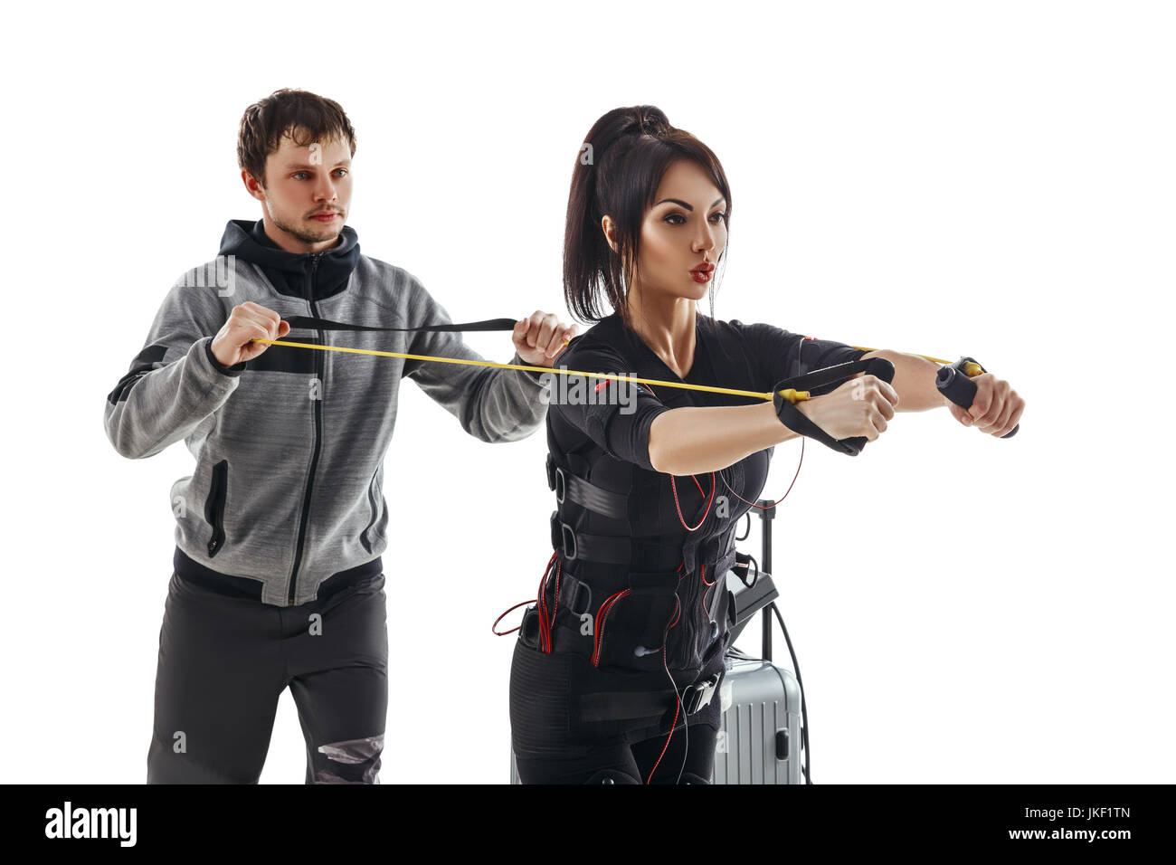 Elettrici di stimolazione muscolare donna fitness in pieno ems tuta torace facendo esercizio di crossover con cavo di formazione. Trainer aiuta a lei. Foto Studio iso Foto Stock