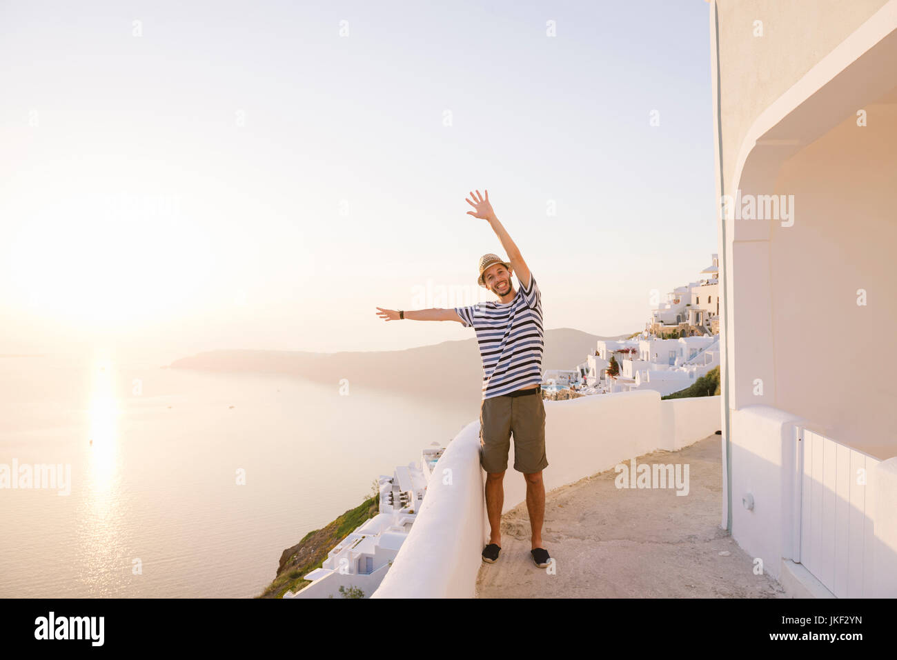 Fira, Santorini, Grecia. Uomo felice in vacanza con le mani in alto godendo il tramonto sul mare Foto Stock