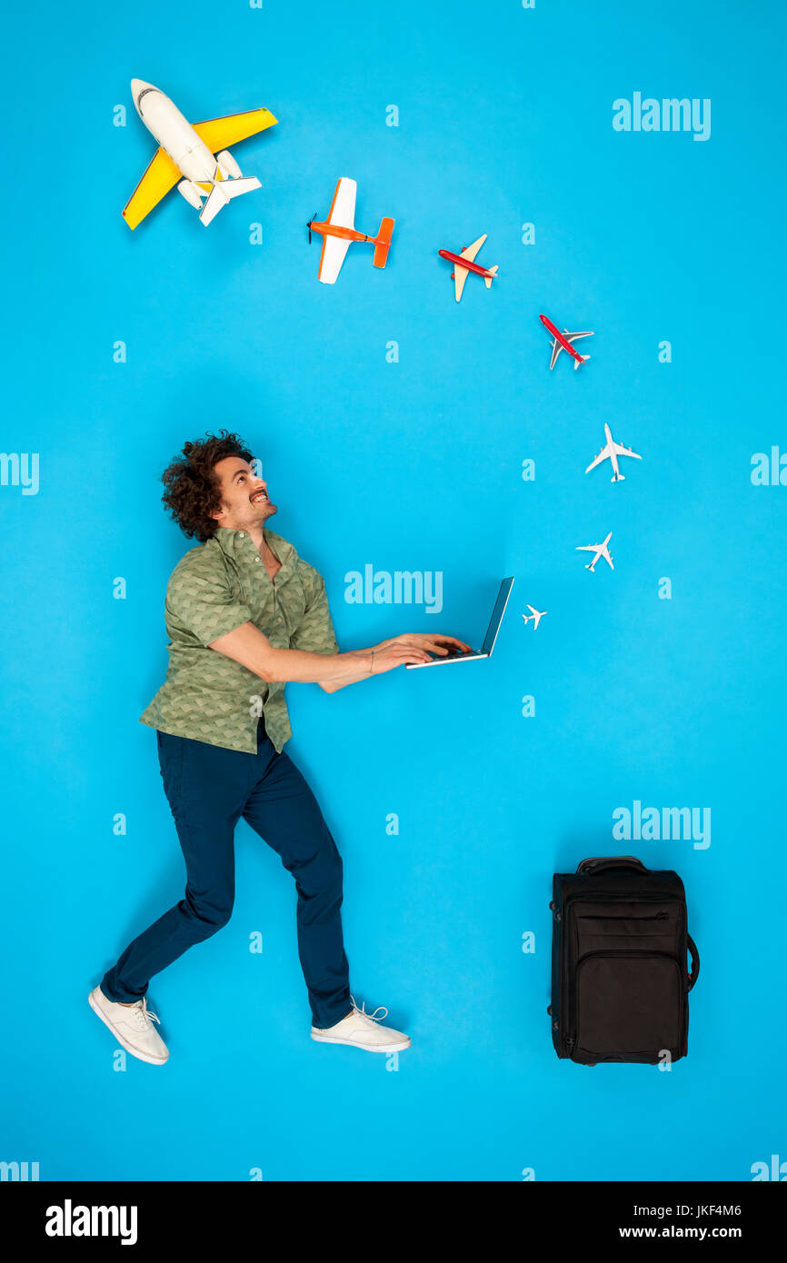 Uomo con valigia guardando gli aerei provenienti dal suo computer portatile Foto Stock
