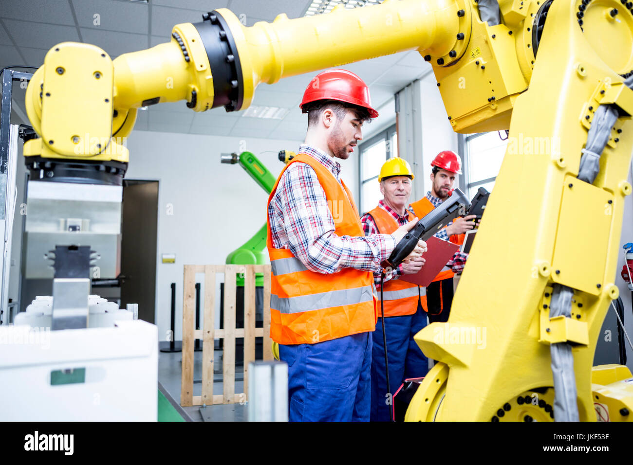 Tre uomini in fabbrica con robot industriale Foto Stock