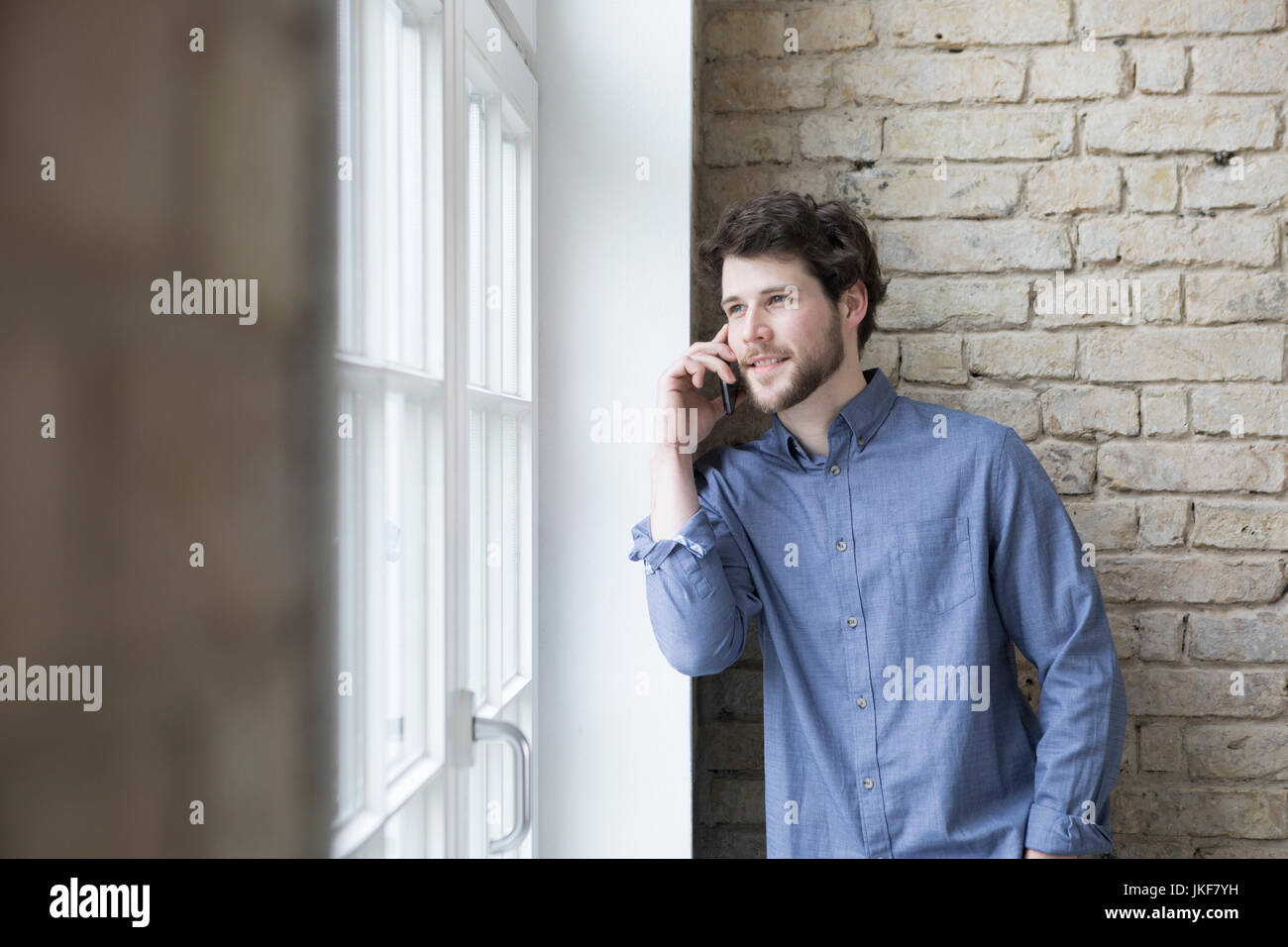 Giovane imprenditore in piedi alla finestra, utilizza lo smartphone Foto Stock