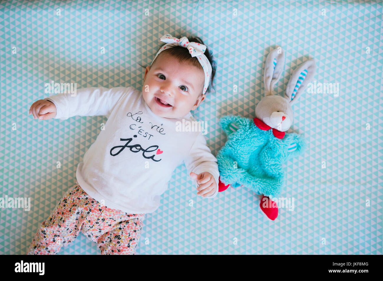 Happy Baby girl sdraiato sul letto accanto a coniglietto giocattolo Foto Stock
