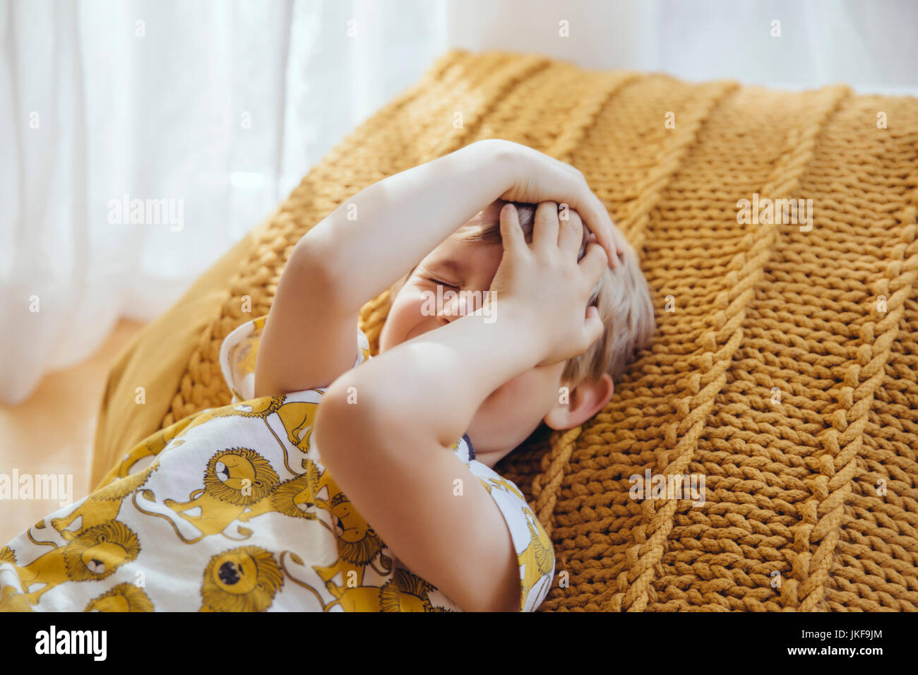 Little Boy giacente sul cuscino che ricopre la faccia con le mani Foto Stock