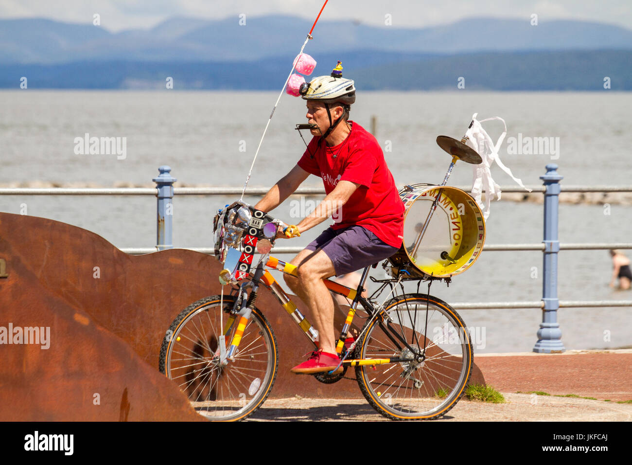 Morecambe, Lancashire, Regno Unito, luglio 2017. Pete Moser, un intrattenitore di strada in bicicletta; gruppi One Man provenienti da tutto il paese convergono sulla Morecambe Promenade per un divertente festival gratuito di caos musicale. La One-man band ha un posto speciale nell'immaginazione di tutti, e questa celebrazione del coordinamento è un evento unico che cattura l'immaginazione delle persone, a prescindere dalla loro età. Una volta visto, mai dimenticato. Le bande sono disponibili in tutte le forme e dimensioni e riproducono musica di ogni genere. Foto Stock