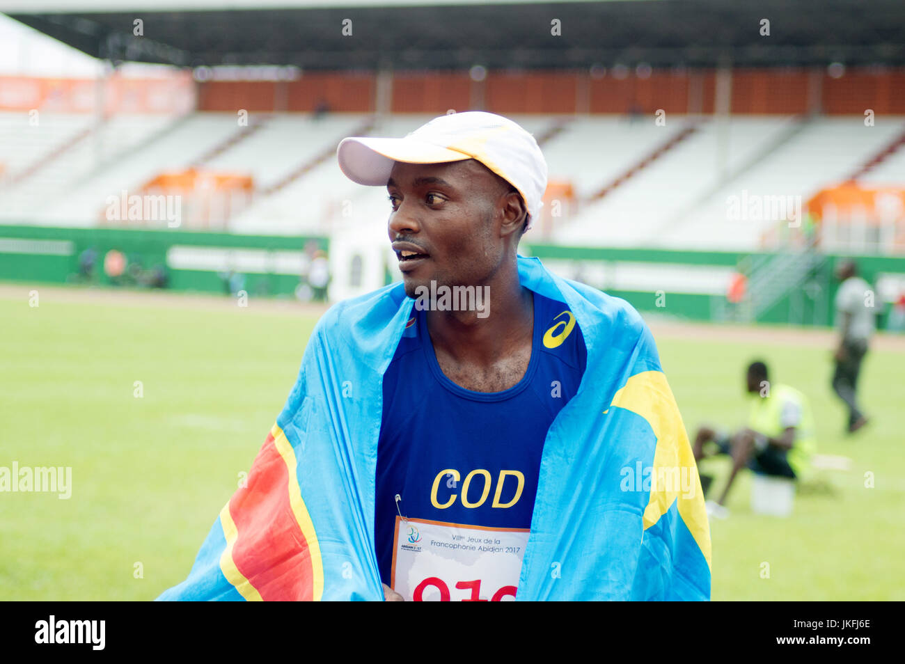 Abidjan, Costa d'Avorio - 23 Luglio 2017: giovani congolesi rider Nako Robondo vincitore della 42km uomo marathon. Indossando una maglietta blu numero 070 e con un cappuccio bianco e coperto con la bandiera del suo paese nel campo sportivo è molto felice. Foto Stock