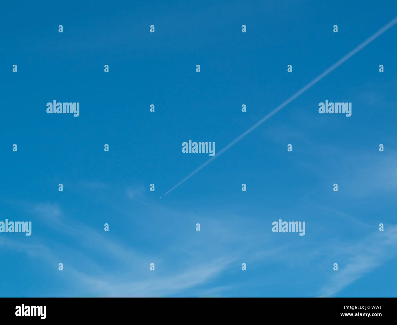 Un cielo blu con un vapore il sentiero che corre attraverso il centro dell'immagine con il velivolo essendo un granello nell'immagine. Foto Stock