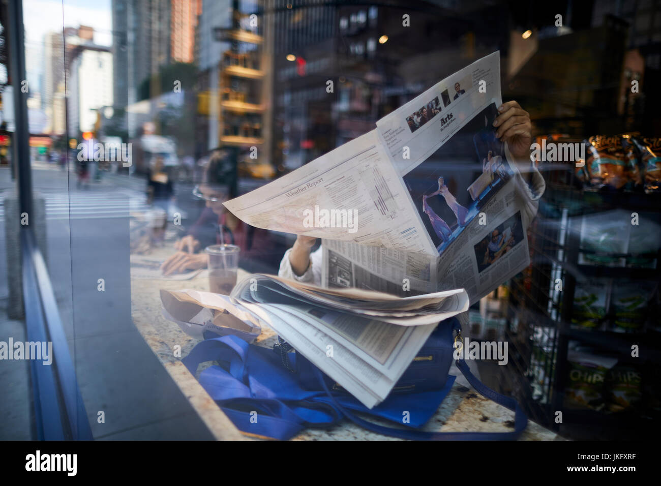 La città di New York Manhattan, la lettura di un quotidiano broadsheet in un coffee shop come Ottava Avenue si riflette nel vetro della finestra Foto Stock