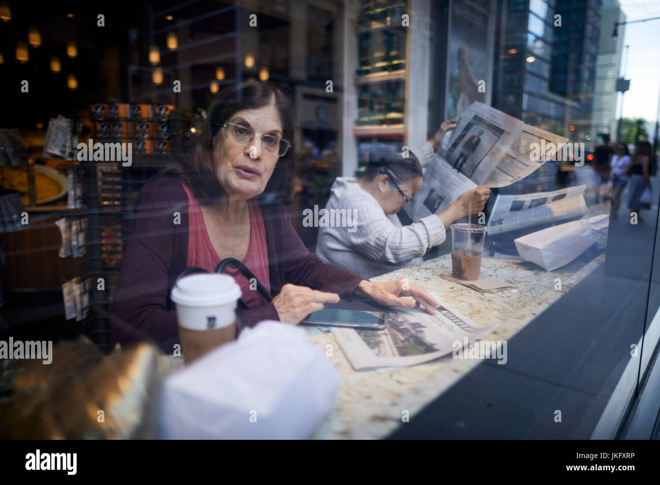 La città di New York Manhattan, la lettura di un quotidiano broadsheet in un coffee shop come Ottava Avenue si riflette nel vetro della finestra Foto Stock