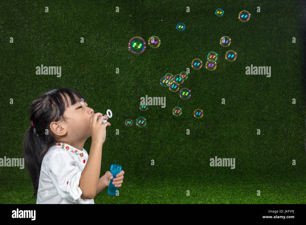 Cinese asiatici bambina soffiando bolle di sapone su erba verde Foto Stock