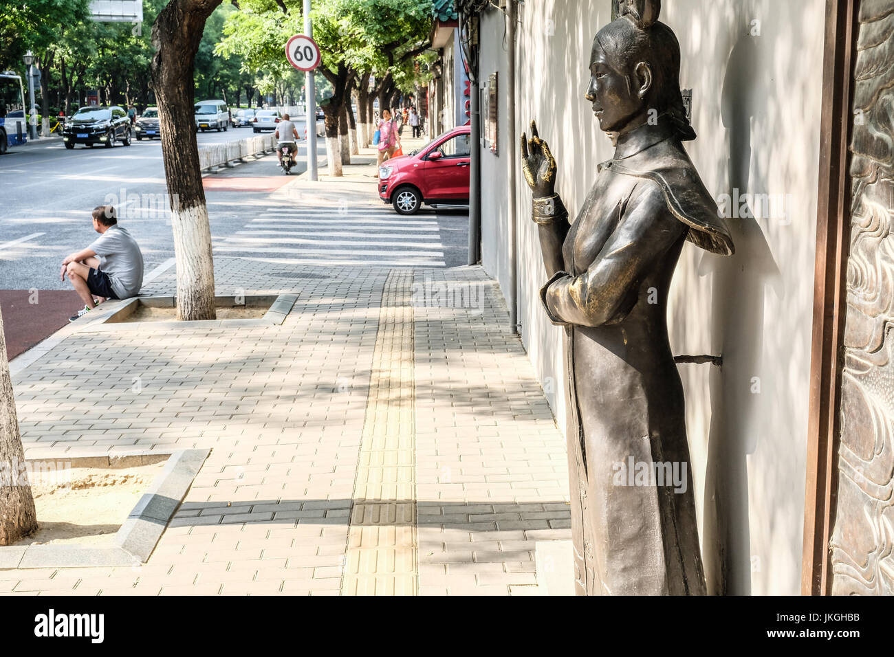 Una femmina marrone statua in cinese tradizionale abito in strada di Pechino con un uomo cinese seduto sul cordolo Foto Stock