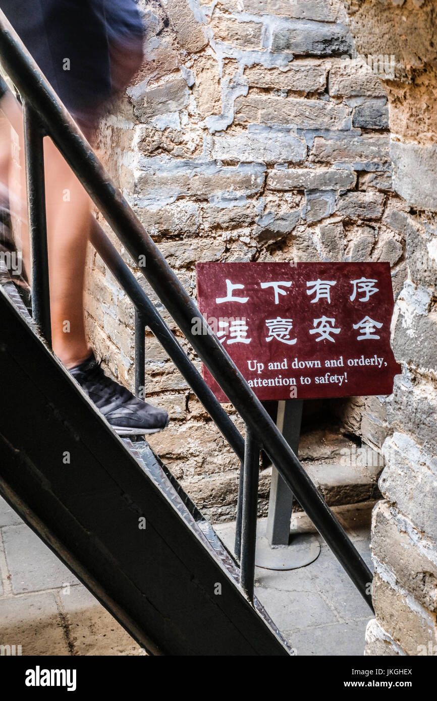 Persone scendendo una ripida rampa di scale di metallo, un cinese e inglese  sicuro segno di avvertimento alla fine Foto stock - Alamy