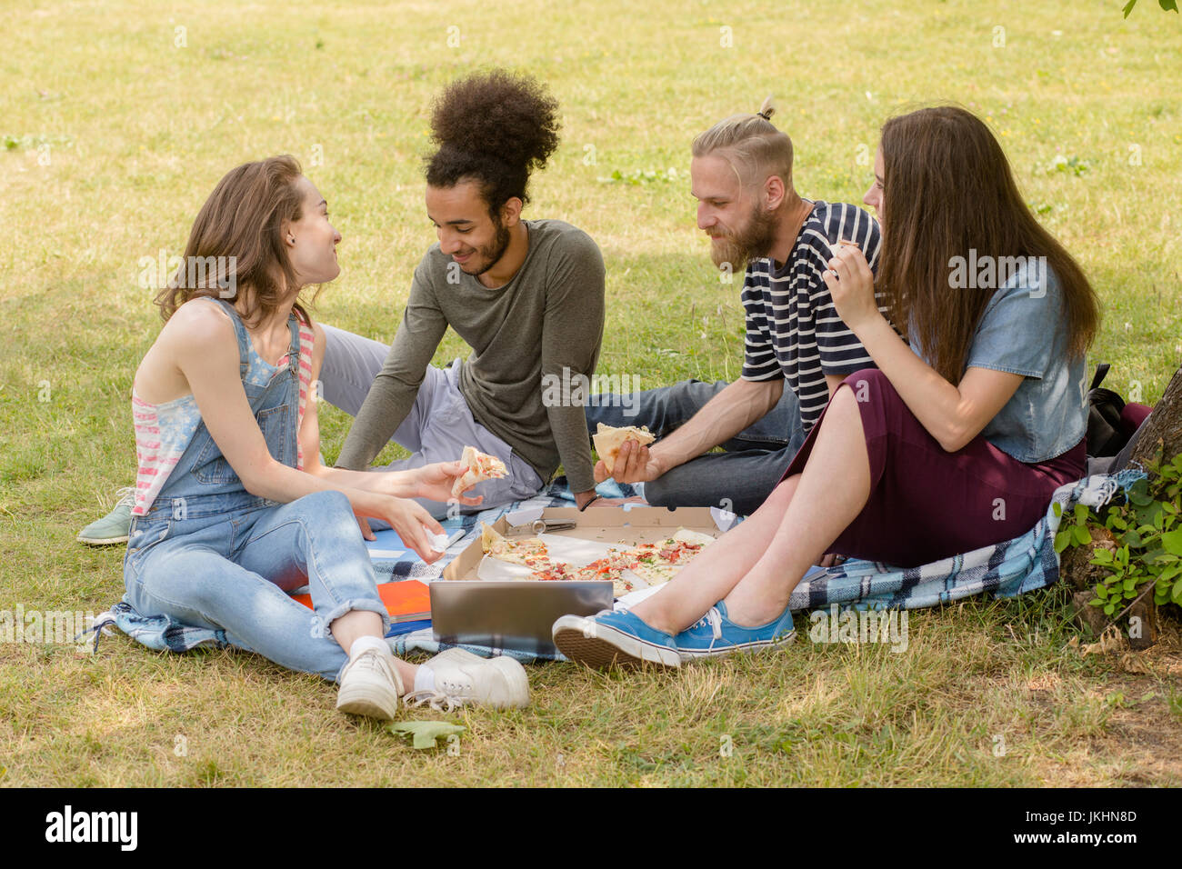 Multietnica giovane gente seduta sul plaid sull'erba mangiando. Foto Stock