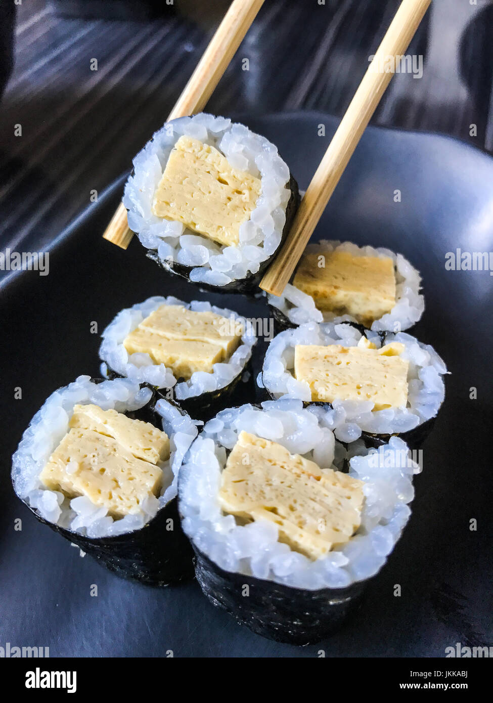 Closeup ritratto di cibo giapponese Tamago nigiri sushi, frittata di uova sushi, sulla piastra nera con bacchette Foto Stock