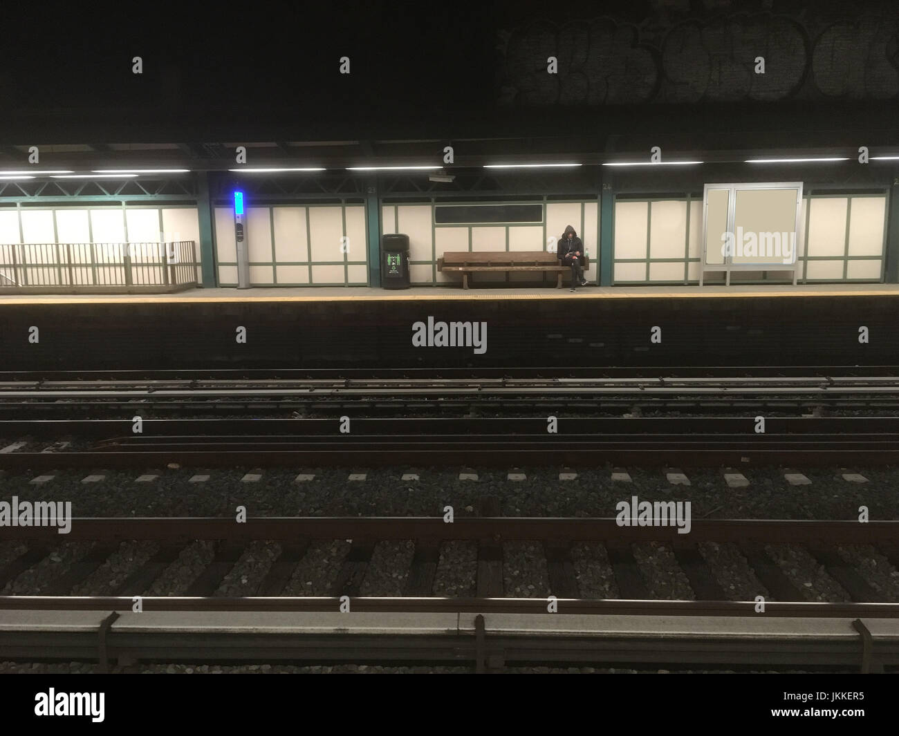 Uomo seduto su una panca di legno in attesa per la metropolitana in ritardo una notte di t. L'uomo attende il treno. New York City i mezzi di trasporto pubblici. Attesa per la metropolitana. Foto Stock