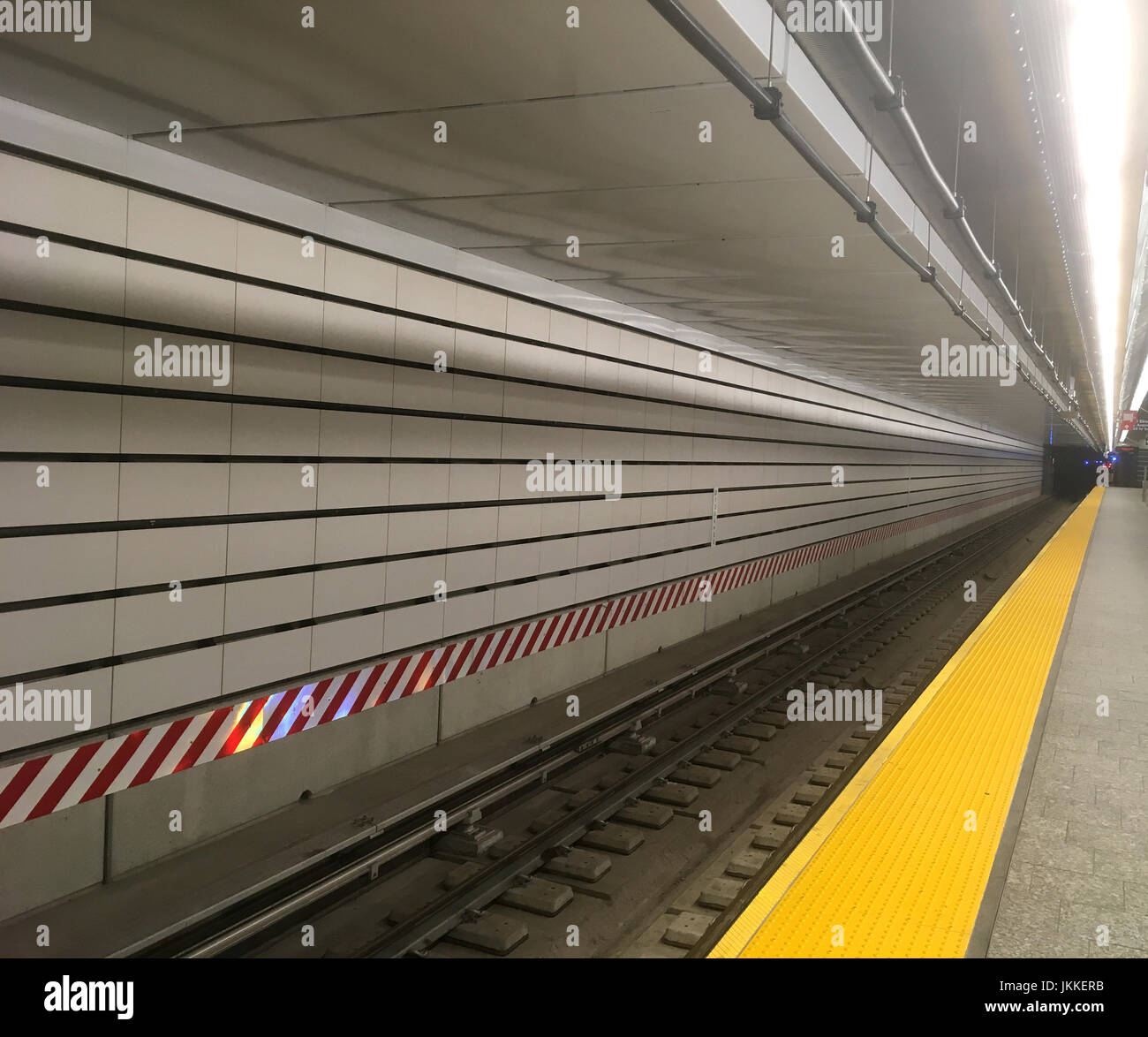 Lunga pista metropolitana che si estende in avanti. Stazione della metropolitana di New York City con piastrelle bianche della metropolitana, avvertimento di pericolo rosso e bianco e binari del treno chiari. Foto Stock
