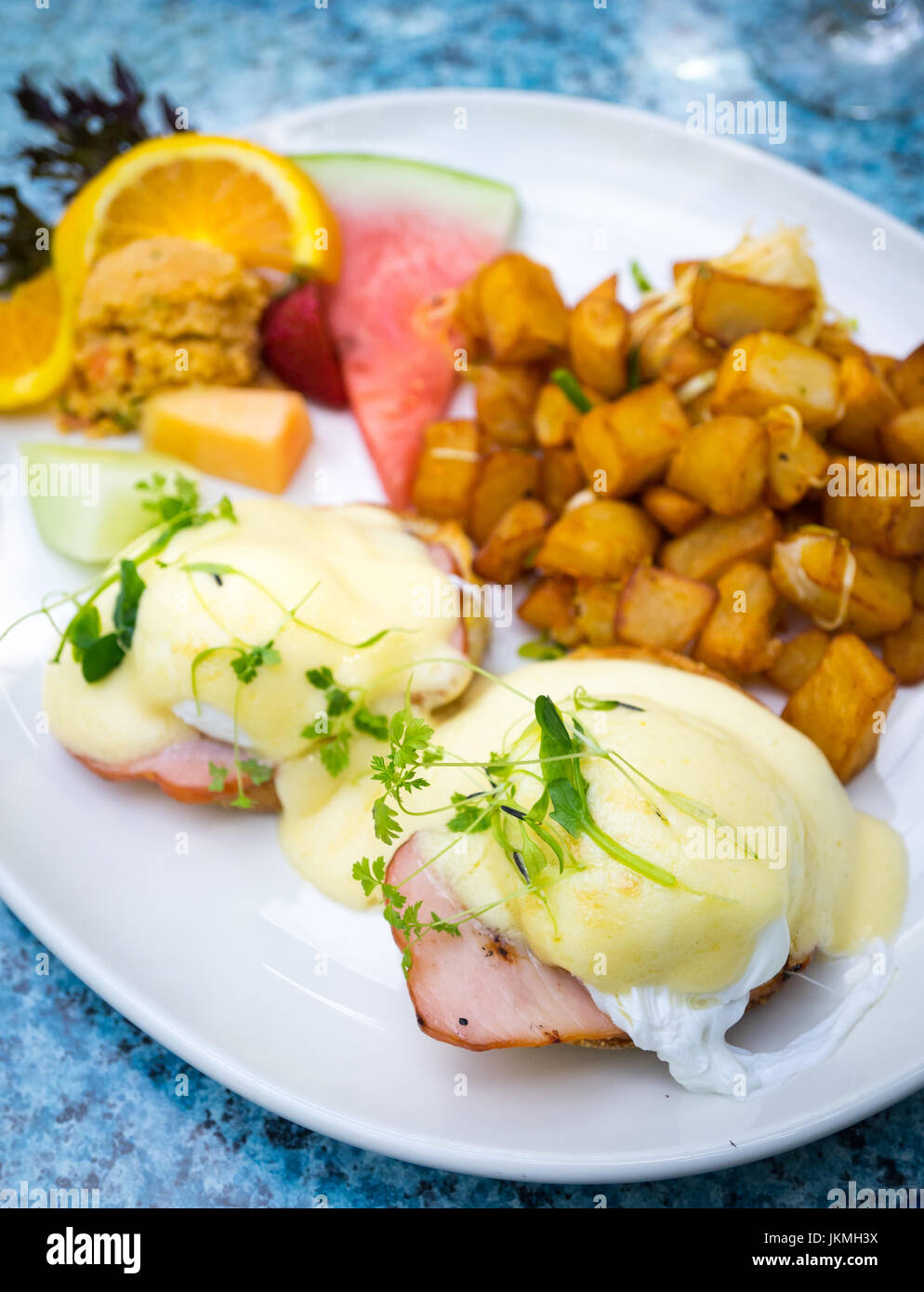 Classic Uova Benedict (soft le uova in camicia, canadese back bacon e salsa olandese su un muffin inglese), patate fritte e frutta per colazione. Foto Stock