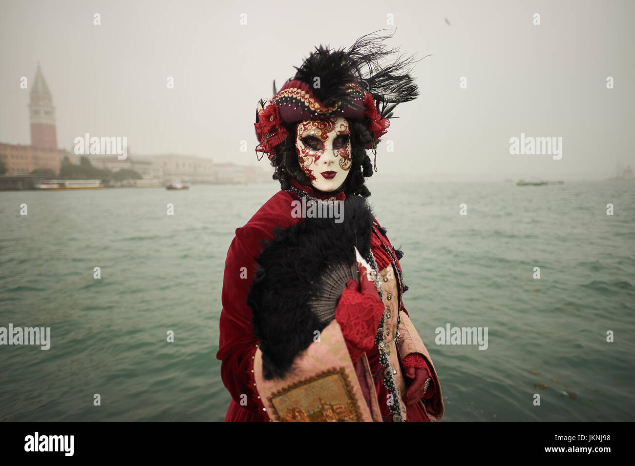 Maschera femminile indossatrice al Carnevale di Venezia con il rivestimento rosso e vestito rosso Foto Stock