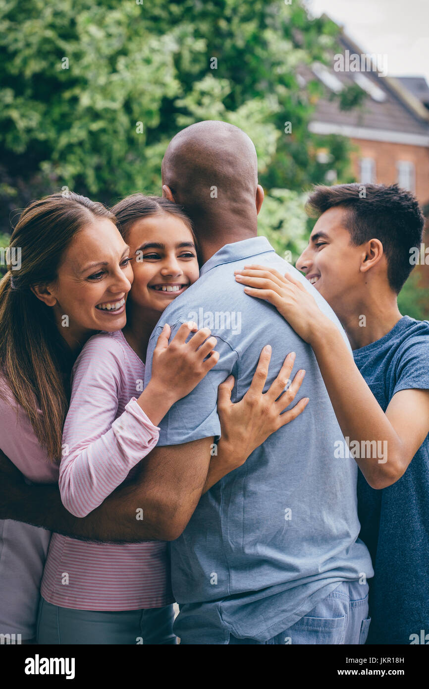 La famiglia felice condivisione di una coccola all'esterno. Tutti si avvolge le loro braccia attorno al padre che ha il suo torna alla fotocamera. Foto Stock