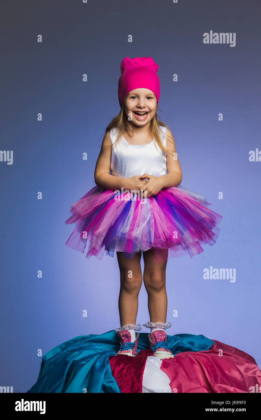 Ritratto di Allegro ragazza indossare gonna in tulle e maglia hat in piedi su tessuti mucchio contro viola b Foto Stock