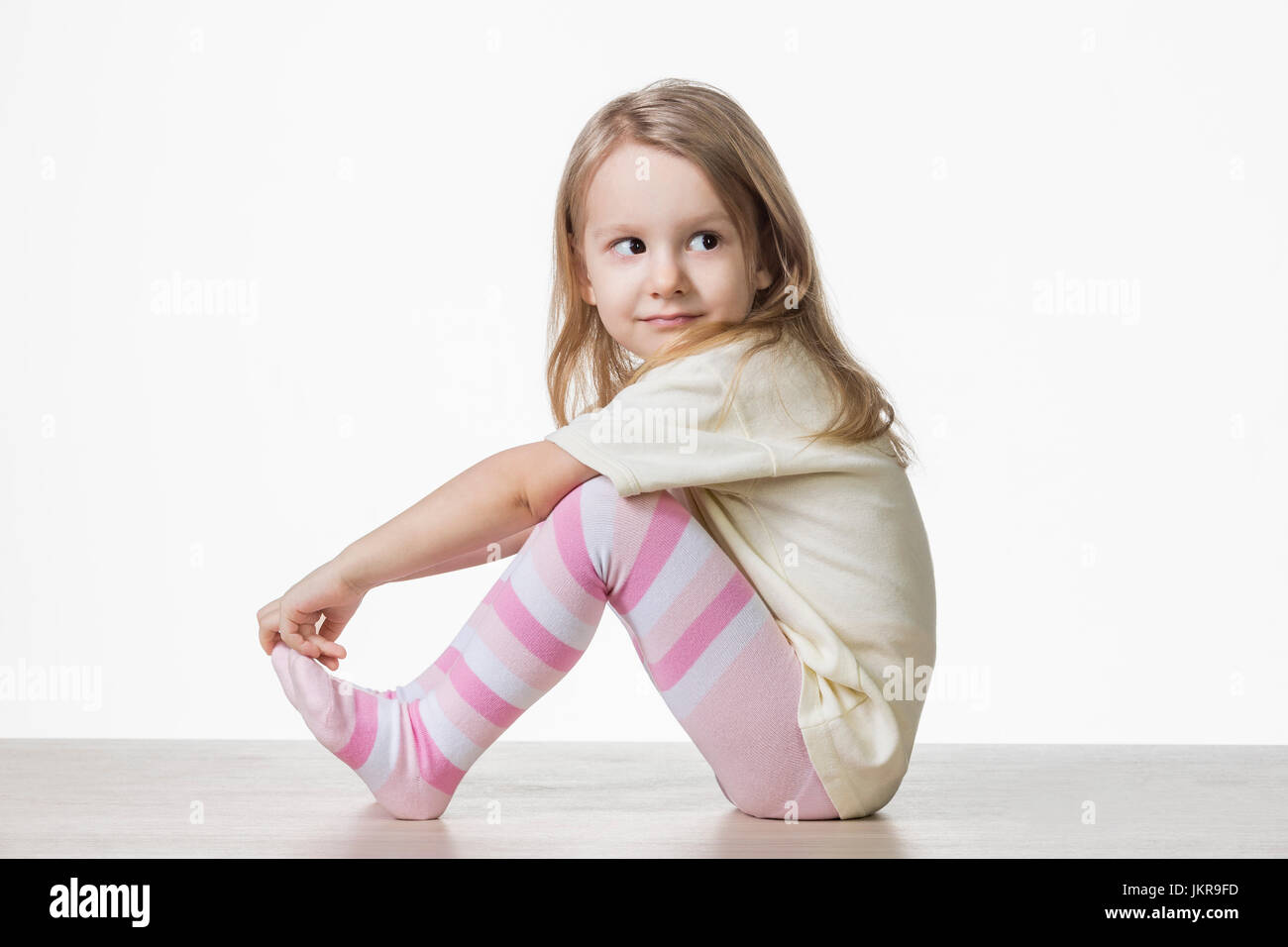 Vista laterale di carino ragazza seduta sul pavimento contro uno sfondo bianco Foto Stock