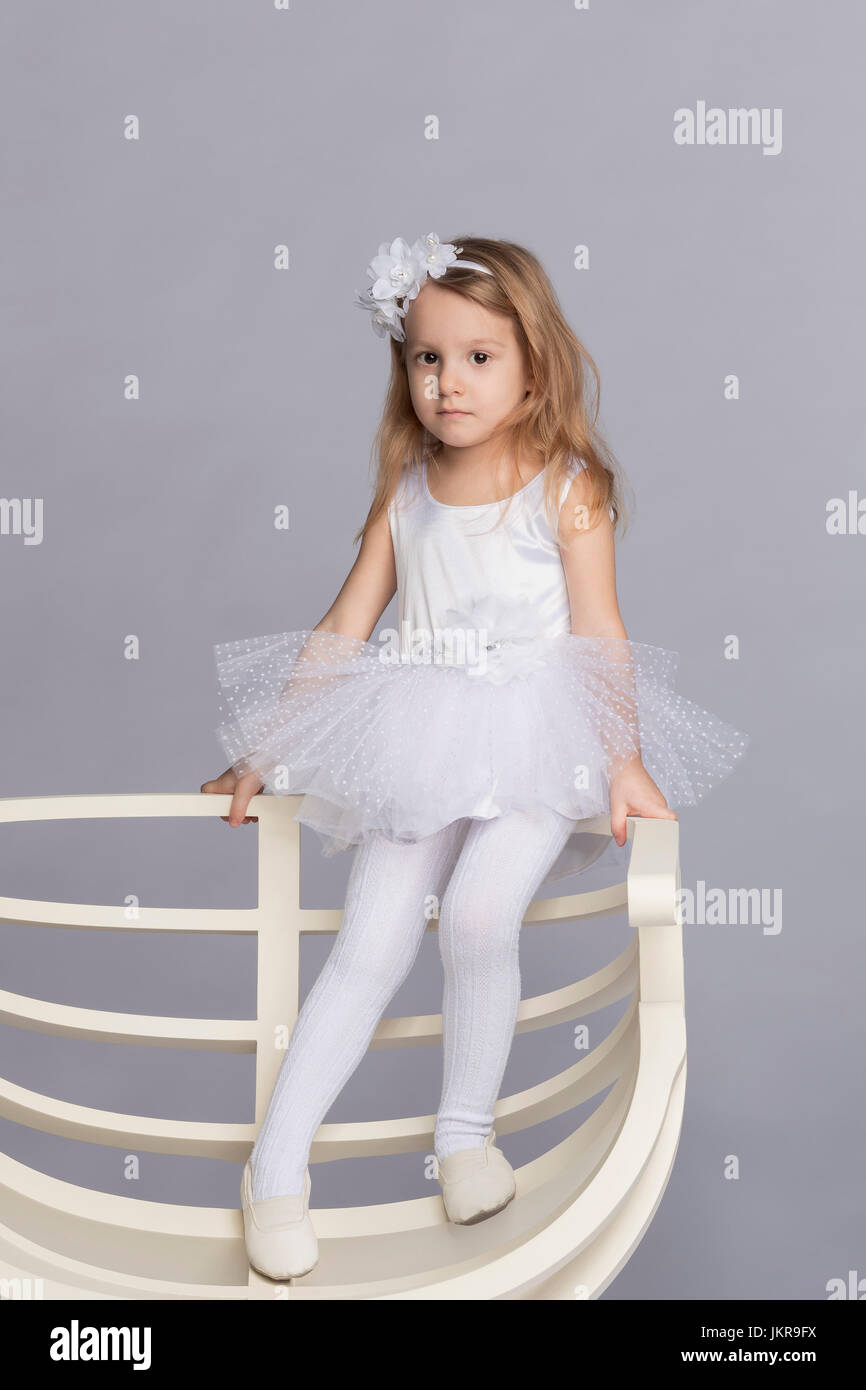 Ritratto di ragazza in piedi sulla sedia bianca contro lo sfondo grigio Foto Stock