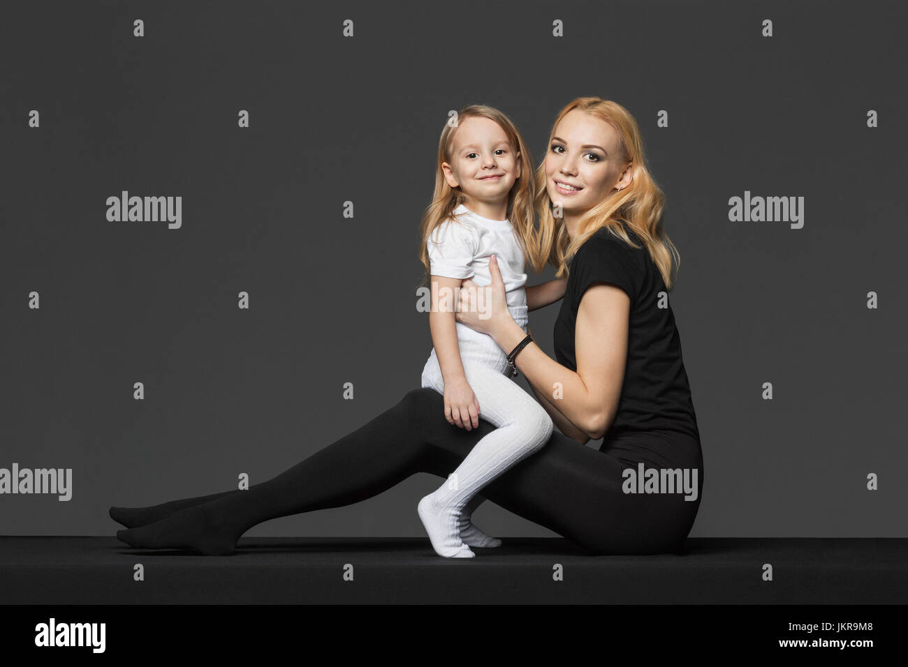 Vista laterale ritratto di madre e figlia seduti contro uno sfondo grigio Foto Stock
