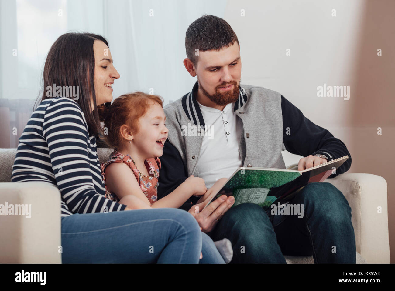 I genitori libro di lettura con la figlia comodamente seduti sul divano di casa Foto Stock