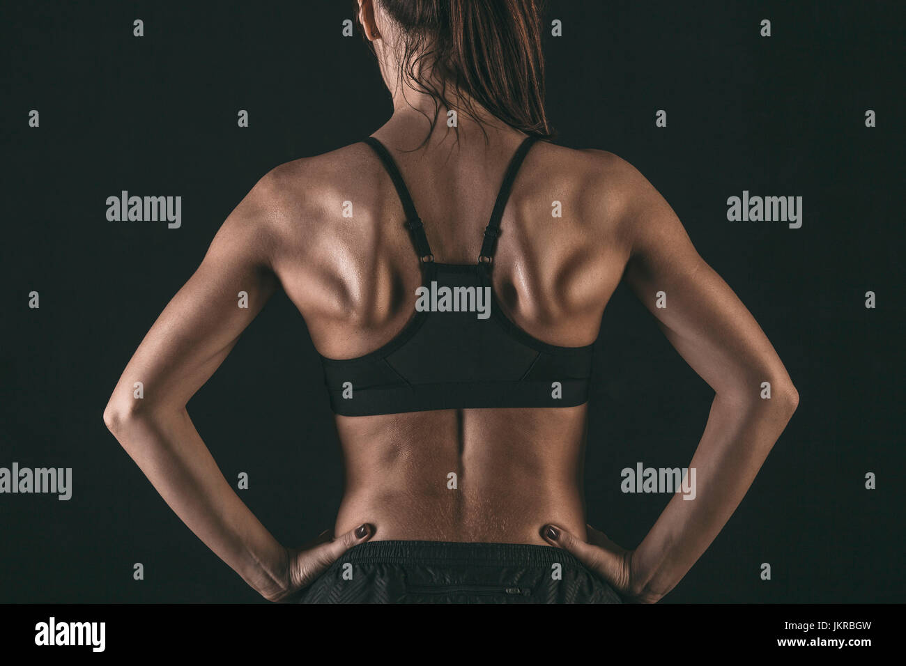 Vista posteriore di atleta donna indossa reggiseno sportivo in piedi con le mani sui hip su sfondo nero Foto Stock
