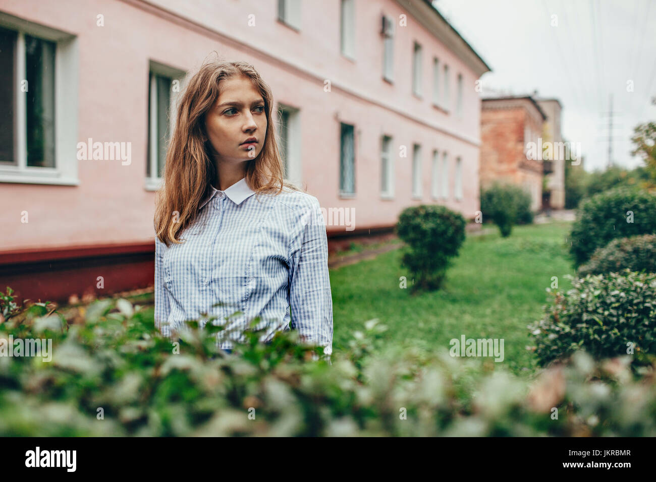 Premurosa ragazza adolescente in piedi da piante contro la costruzione di Foto Stock