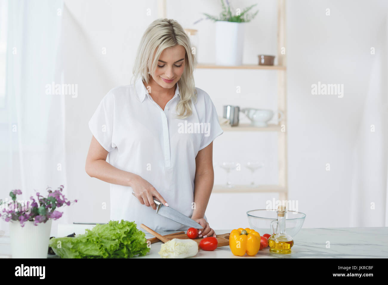 Sorridente giovane donna Tritare i pomodori sul tagliere in cucina Foto Stock