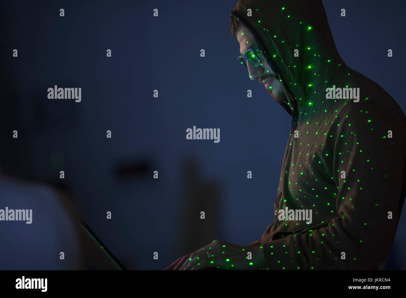 Luci verdi su computer hacker indossando maglietta con cappuccio utilizzando laptop Foto Stock