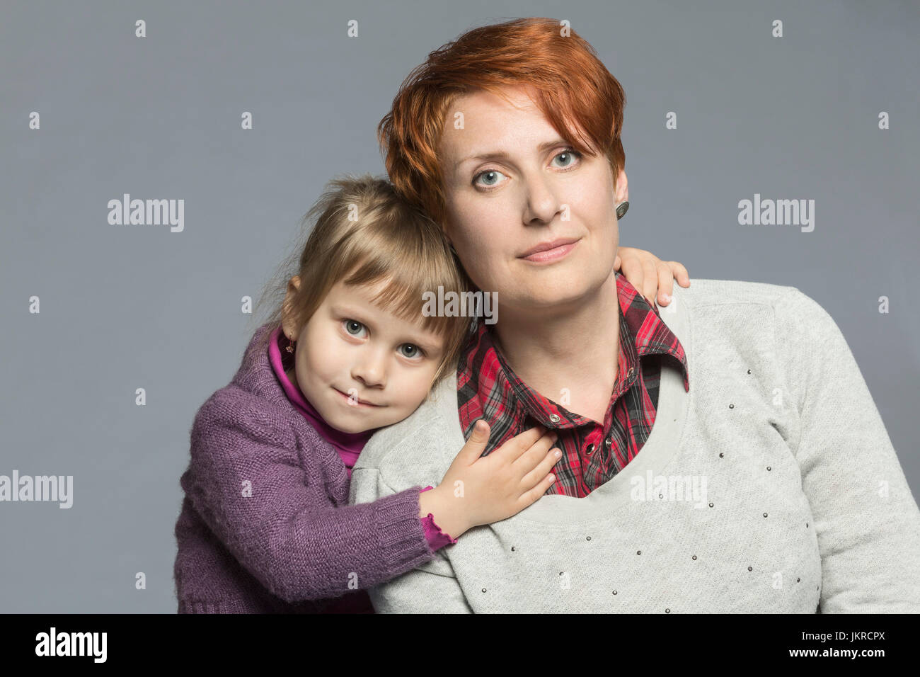 Ritratto della figlia abbracciando la madre contro lo sfondo grigio Foto Stock