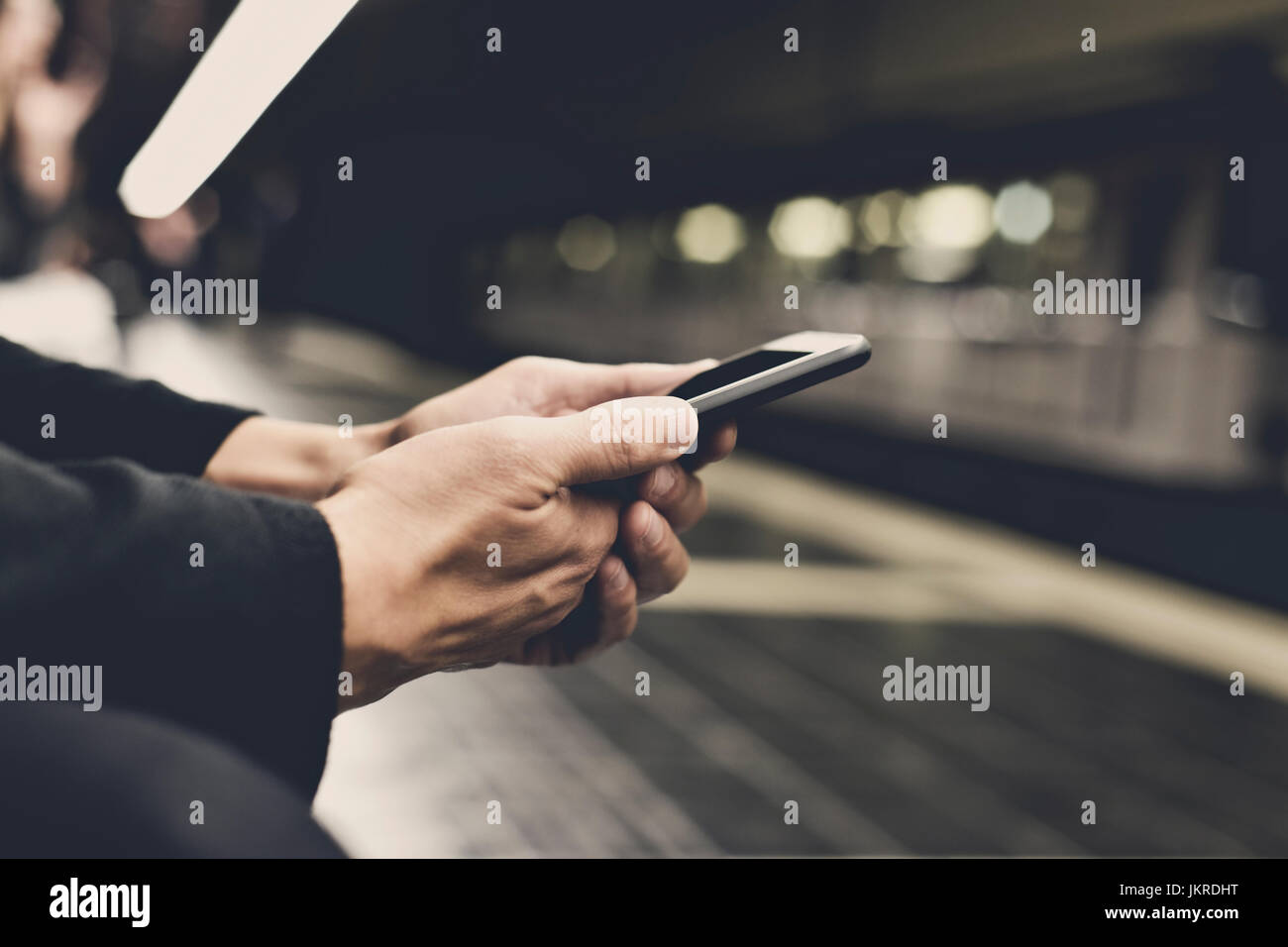 Primo piano di un giovane uomo caucasico utilizzando uno smartphone in un treno della metropolitana o tram station, filtrata Foto Stock