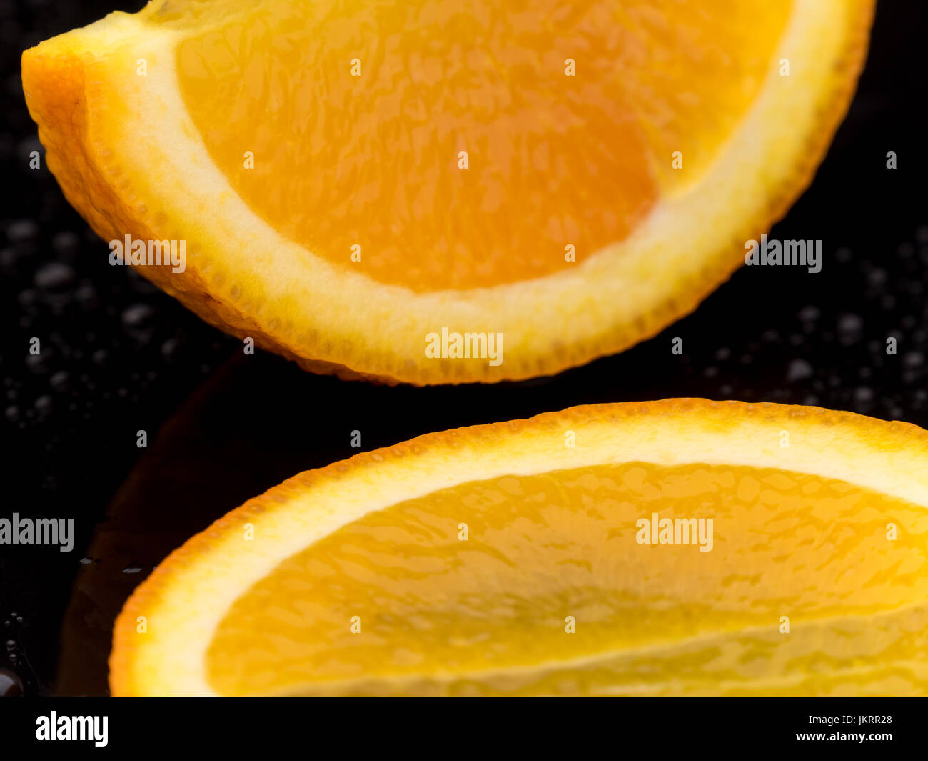 Close-up di frutta arancione nero a superficie riflettente con goccioline di acqua Foto Stock