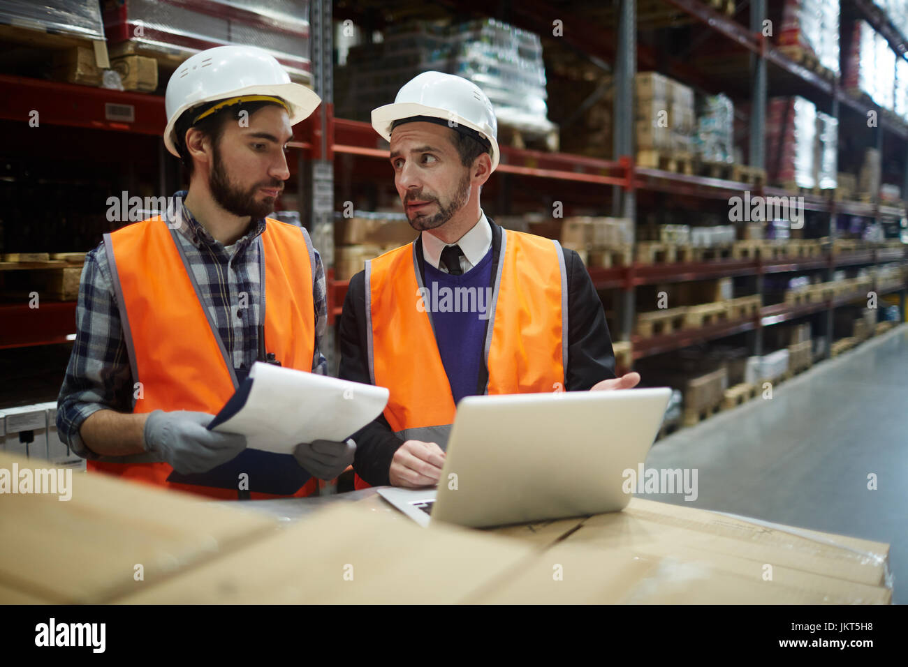 Ritratto di due magazzinieri facendo inventario di magazzino, manager di parlare al caricatore durante l'utilizzo di laptop per immettere dati relativi a beni inventario elenca i Foto Stock
